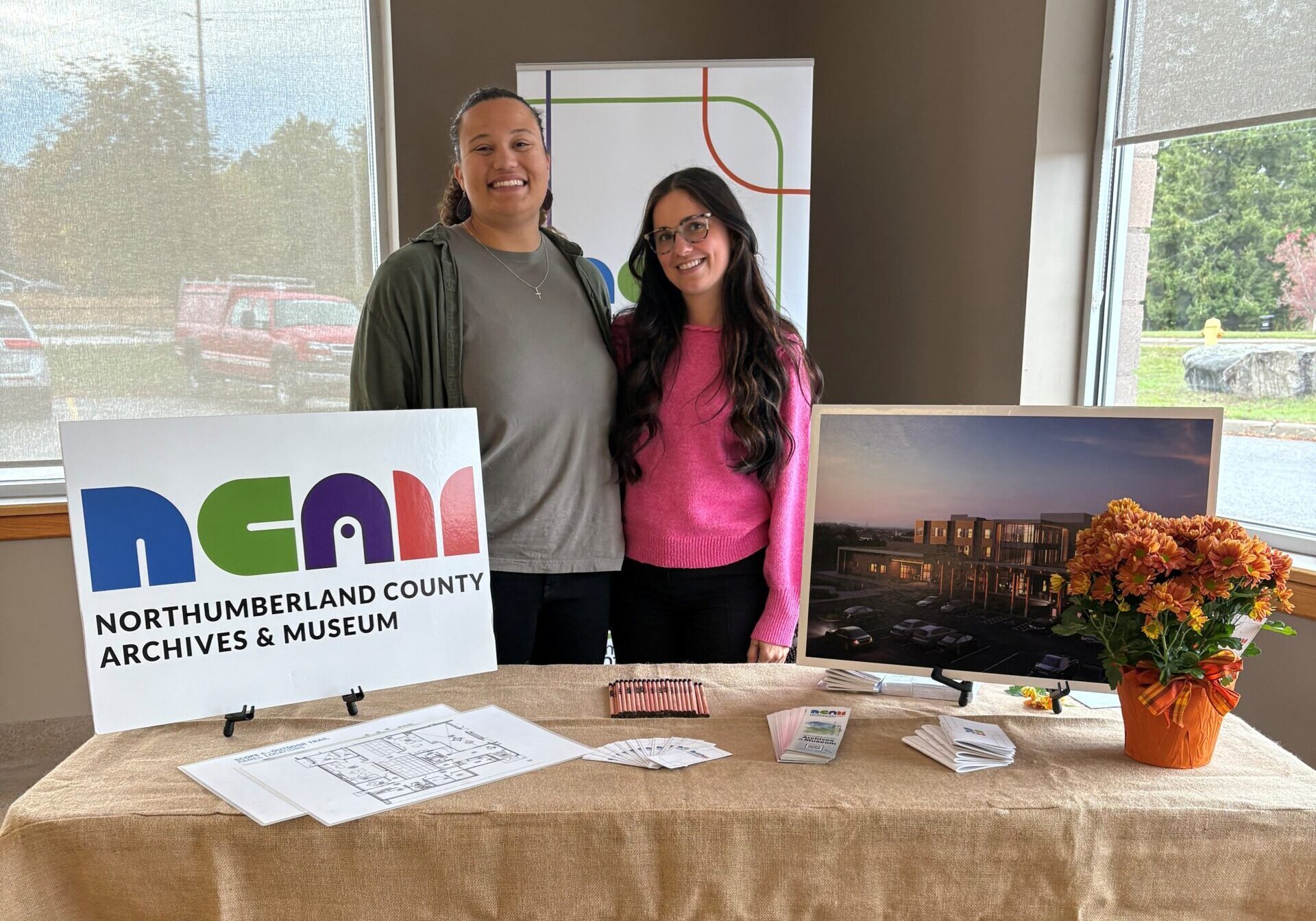 NCAM staff smile, standing behind tradeshow booth