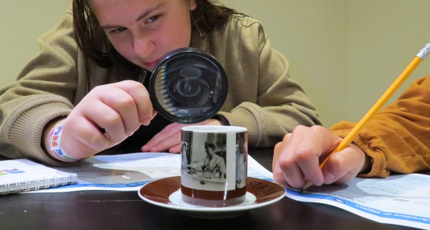 Young girl looking at an older teacup through a magnifying glass.