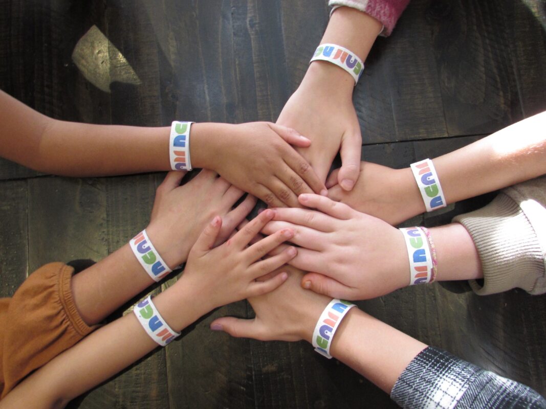 Kids put their hands together, wearing NCAM bracelets